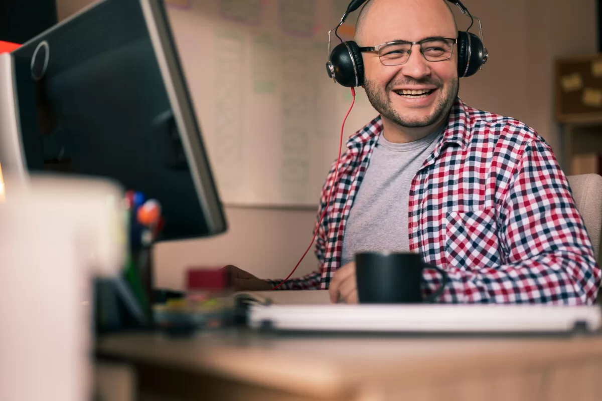 Smiling man with headphones at computer desk.