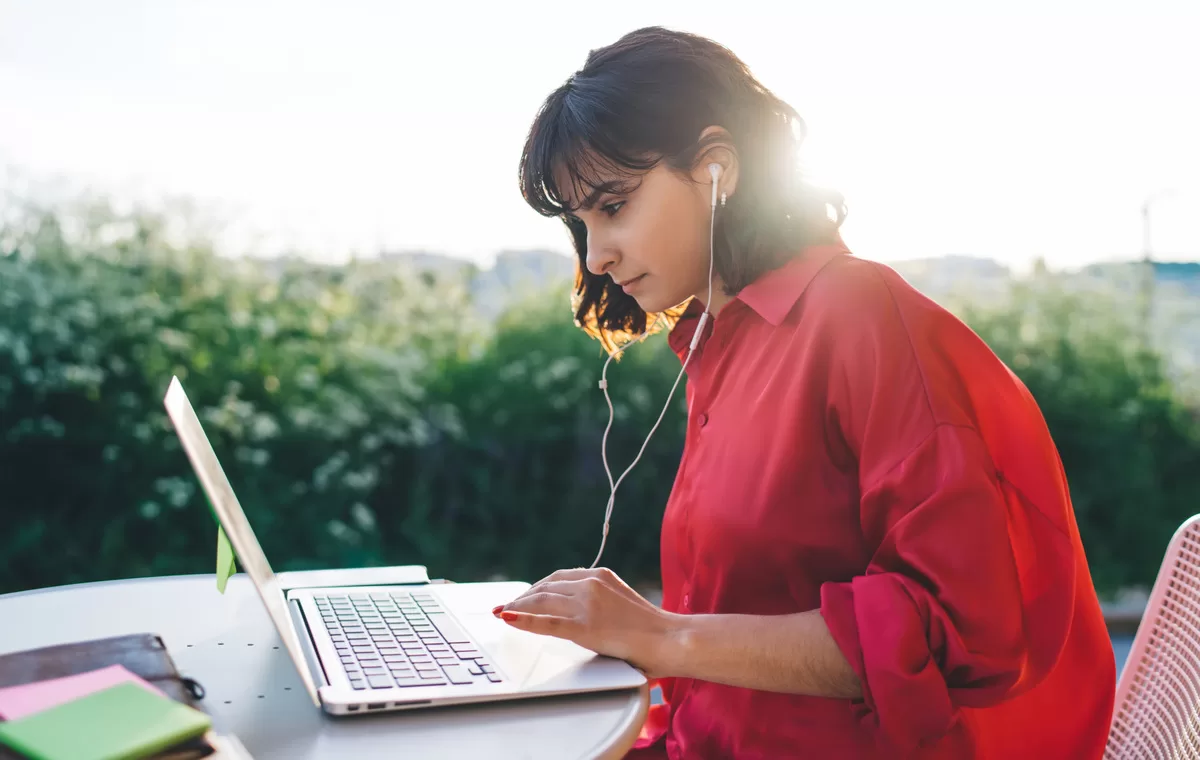 Woman working on laptop outdoors with headphones