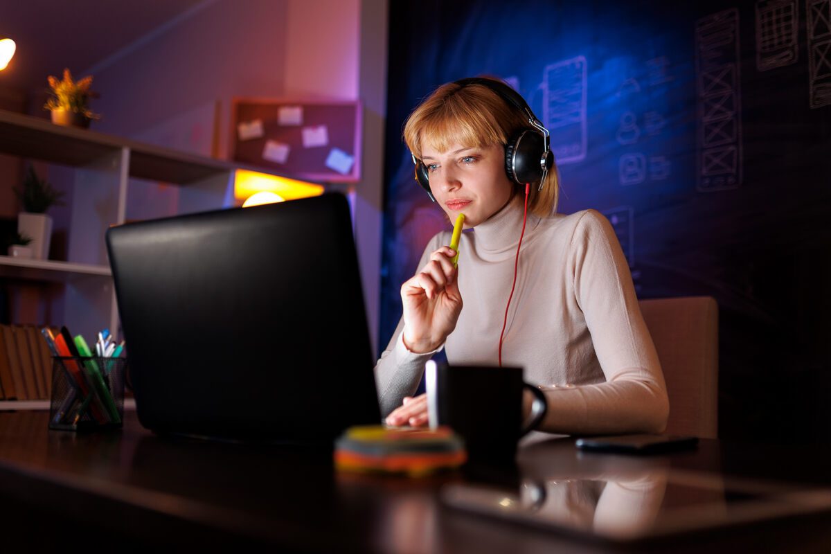 Focused woman working late at computer with headphones.
