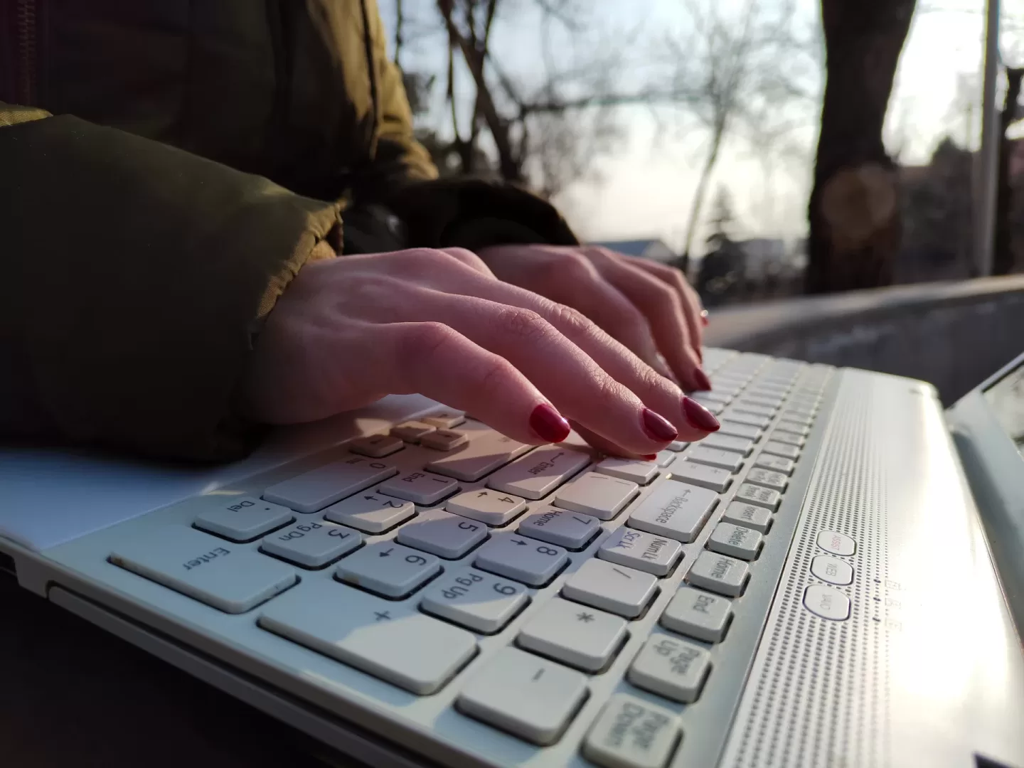 Hands typing on laptop outdoors, red nails visible.