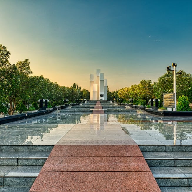 Granite pathway with steps among lush green trees leading to modern tall building in national main heroes cemetery in Kalibata